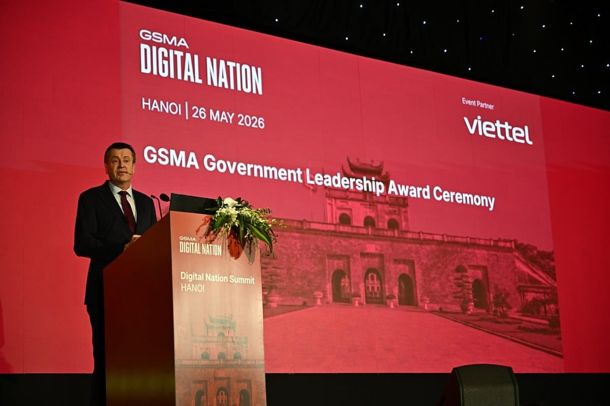 Diễn giả vest đen, cà vạt đỏ phát biểu tại hội nghị GSMA Digital Nation, nền đỏ logo Viettel.