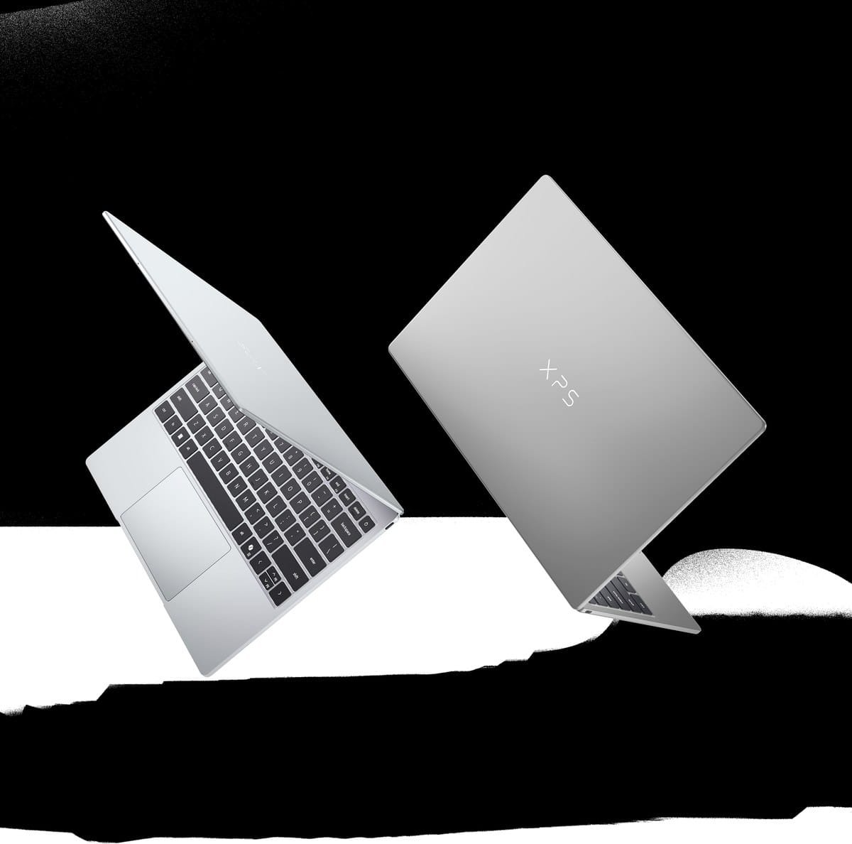 Hai chiếc laptop Dell XPS màu bạc trên nền đen, một chiếc mở màn hình sáng xanh.