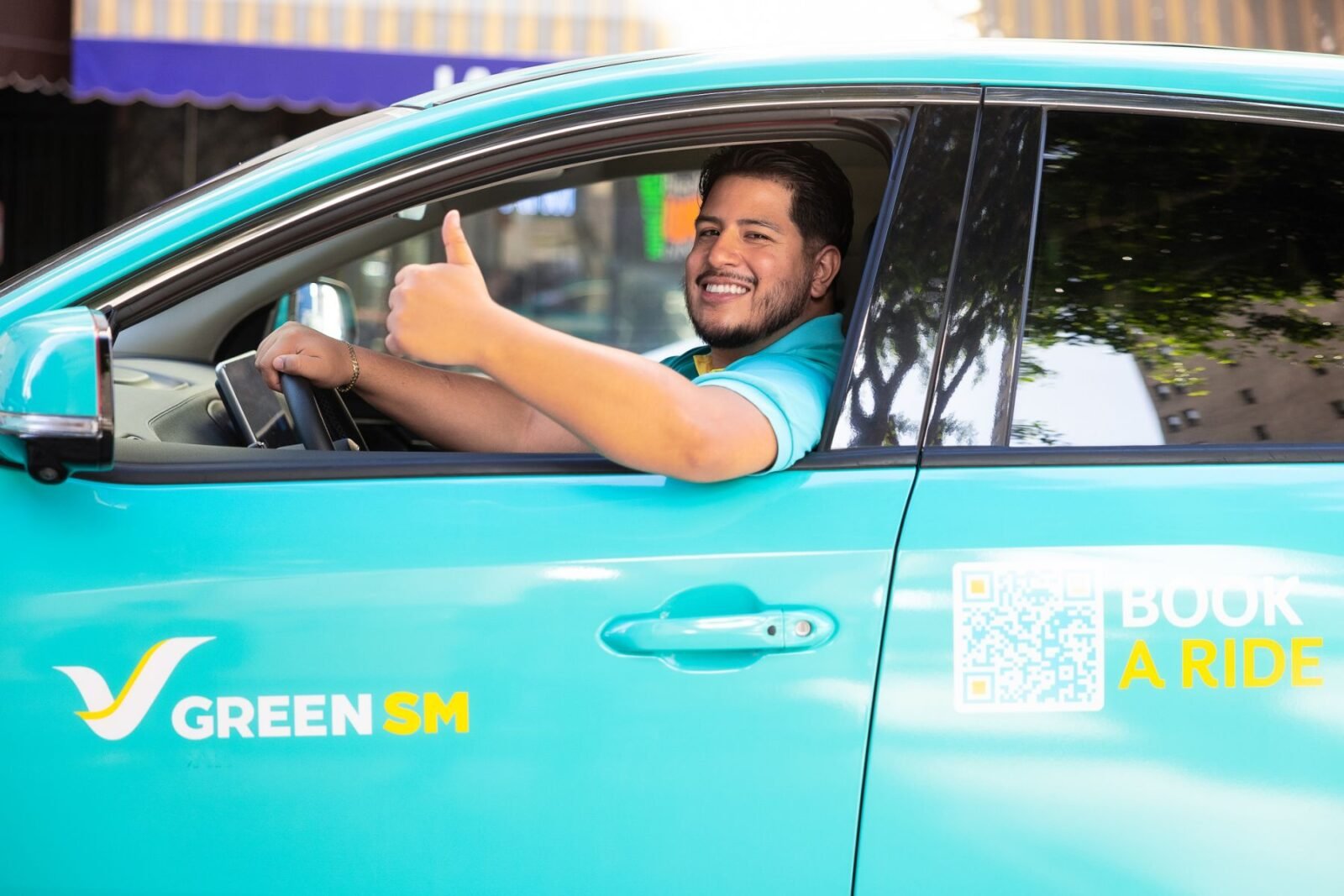 Tài xế Green SM mỉm cười sau tay lái chiếc VinFast VF 8 màu xanh cyan tại Los Angeles