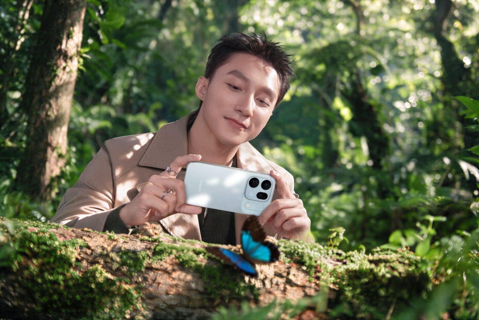 Sơn Tùng M-TP cầm chiếc OPPO Find X10 màu trắng chụp một con bướm xanh đậu trên thân cây phủ rêu trong rừng