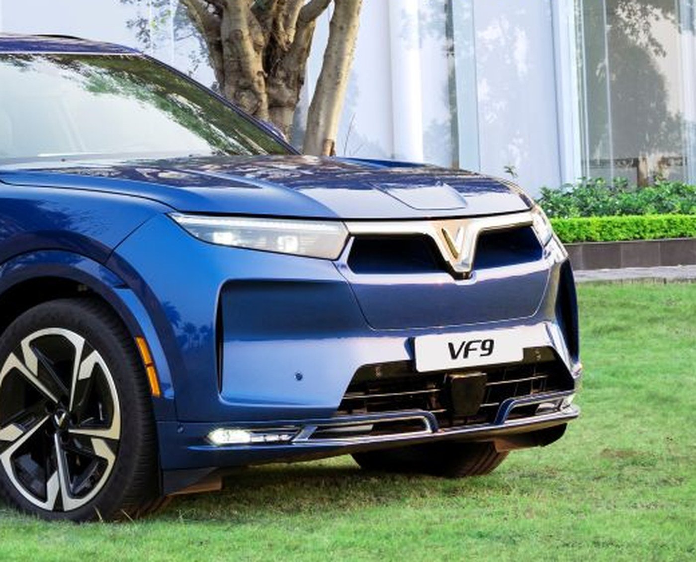 Cận cảnh đầu xe VinFast VF 9 với biểu tượng chữ V mạ sáng, cụm đèn trước và biển tên VF 9