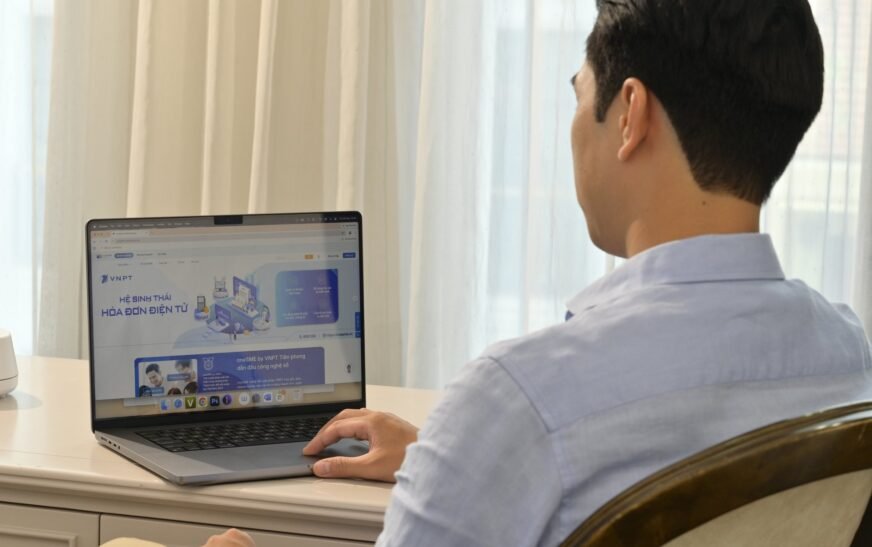 Người dùng ngồi tại bàn làm việc, mở laptop hiển thị trang hệ sinh thái hóa đơn điện tử của VNPT